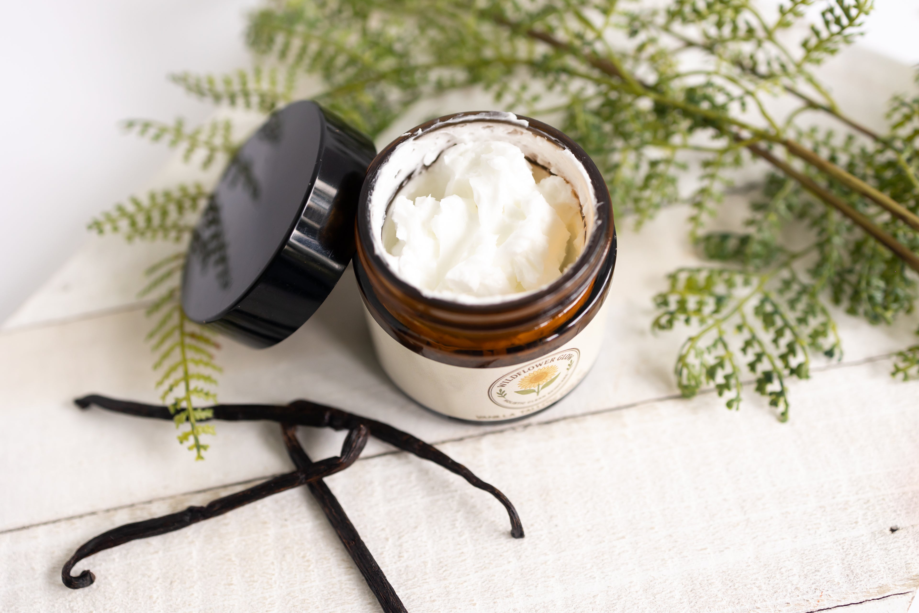 Jar of cream with a black lid on a white surface with greenery