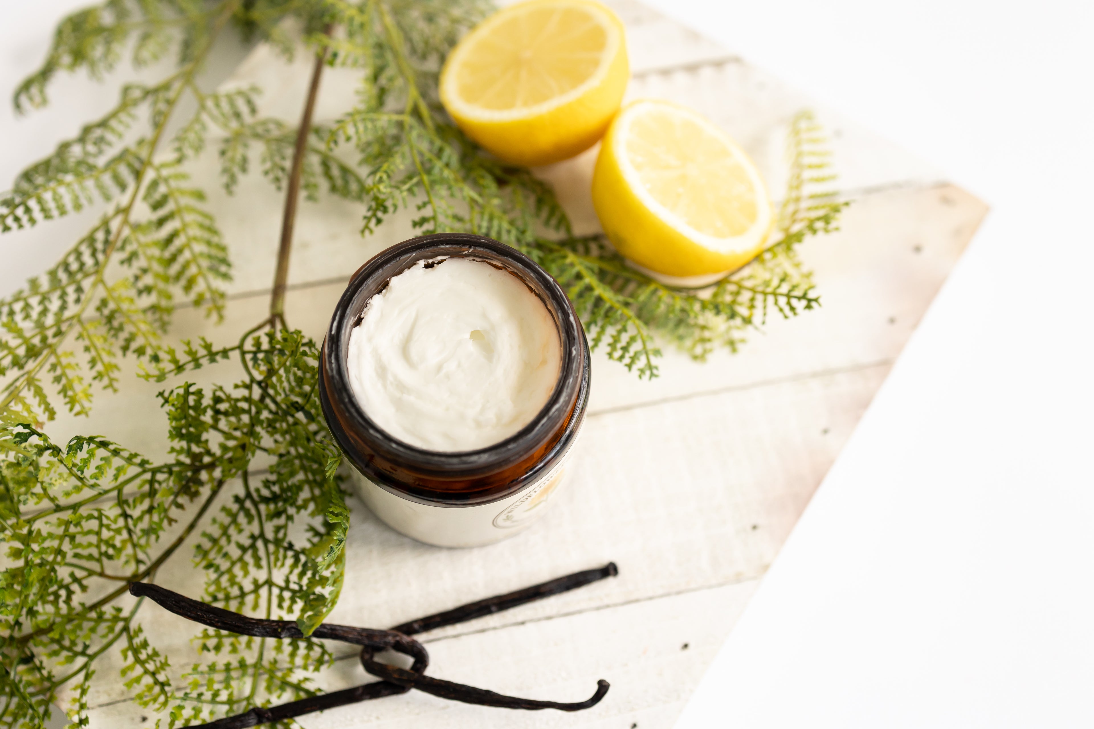 Jar of cream with lemons and vanilla bean on a white background