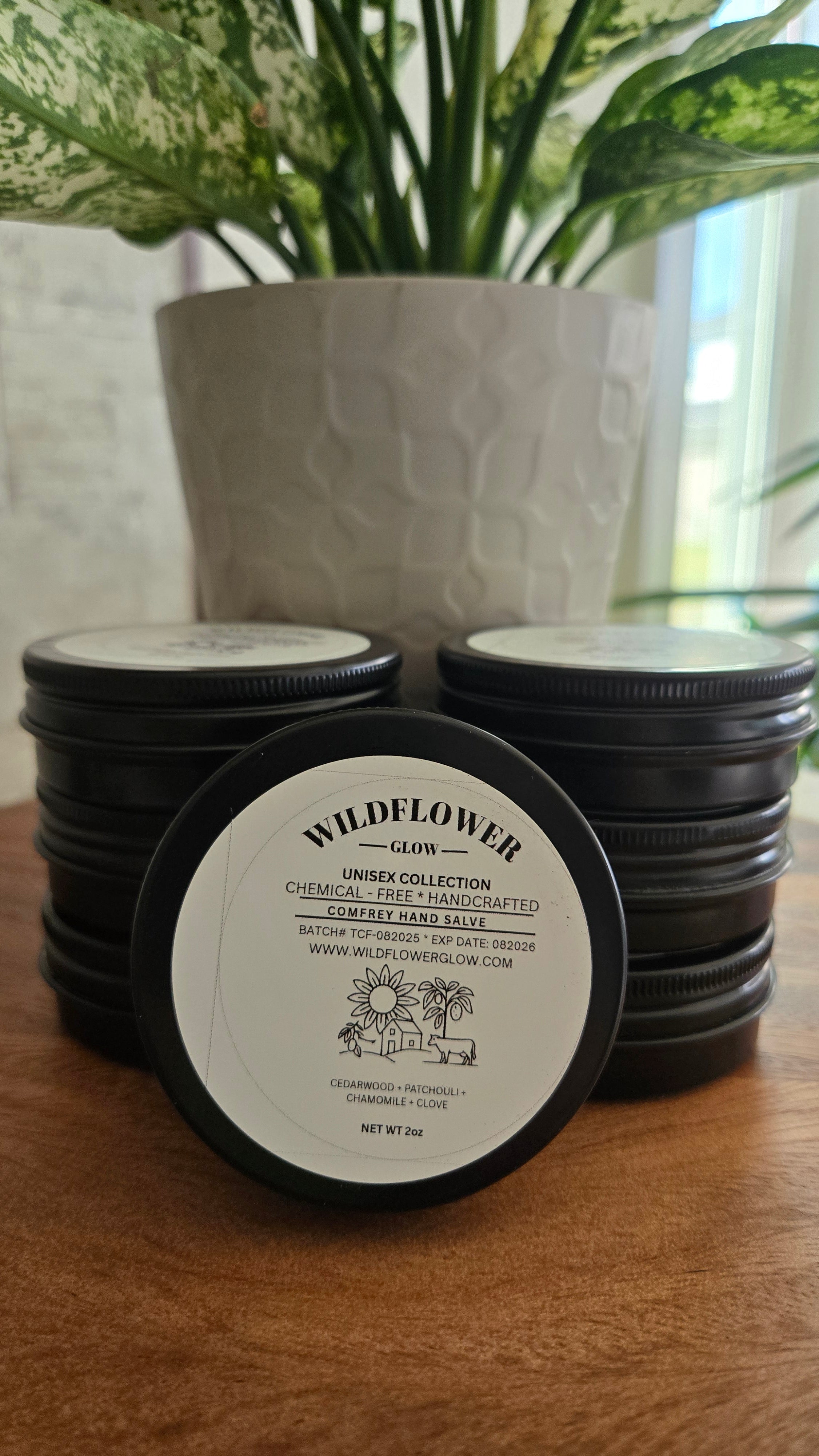 Black tins with the Wildflower Glow logo on a wooden surface next to a plant