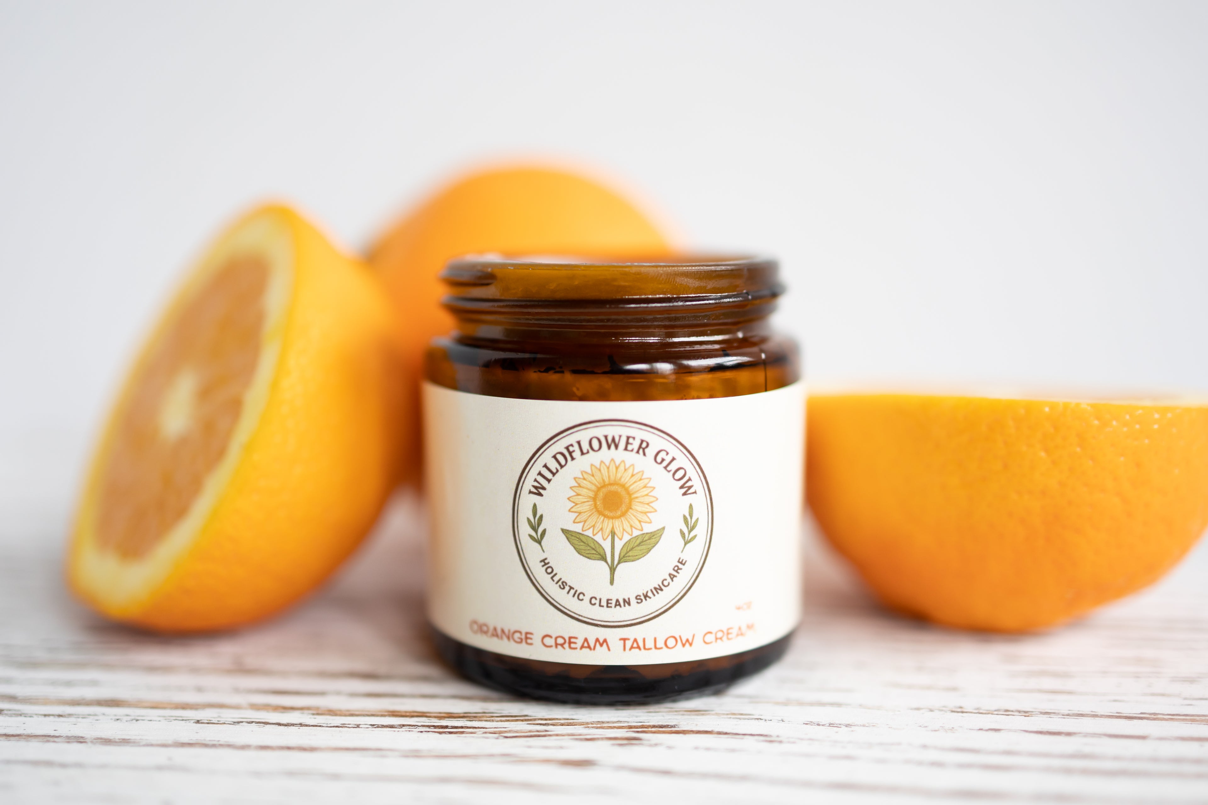 Jar of Wildflower Glow Orange Cream Tallow Creme with oranges on a light wooden surface