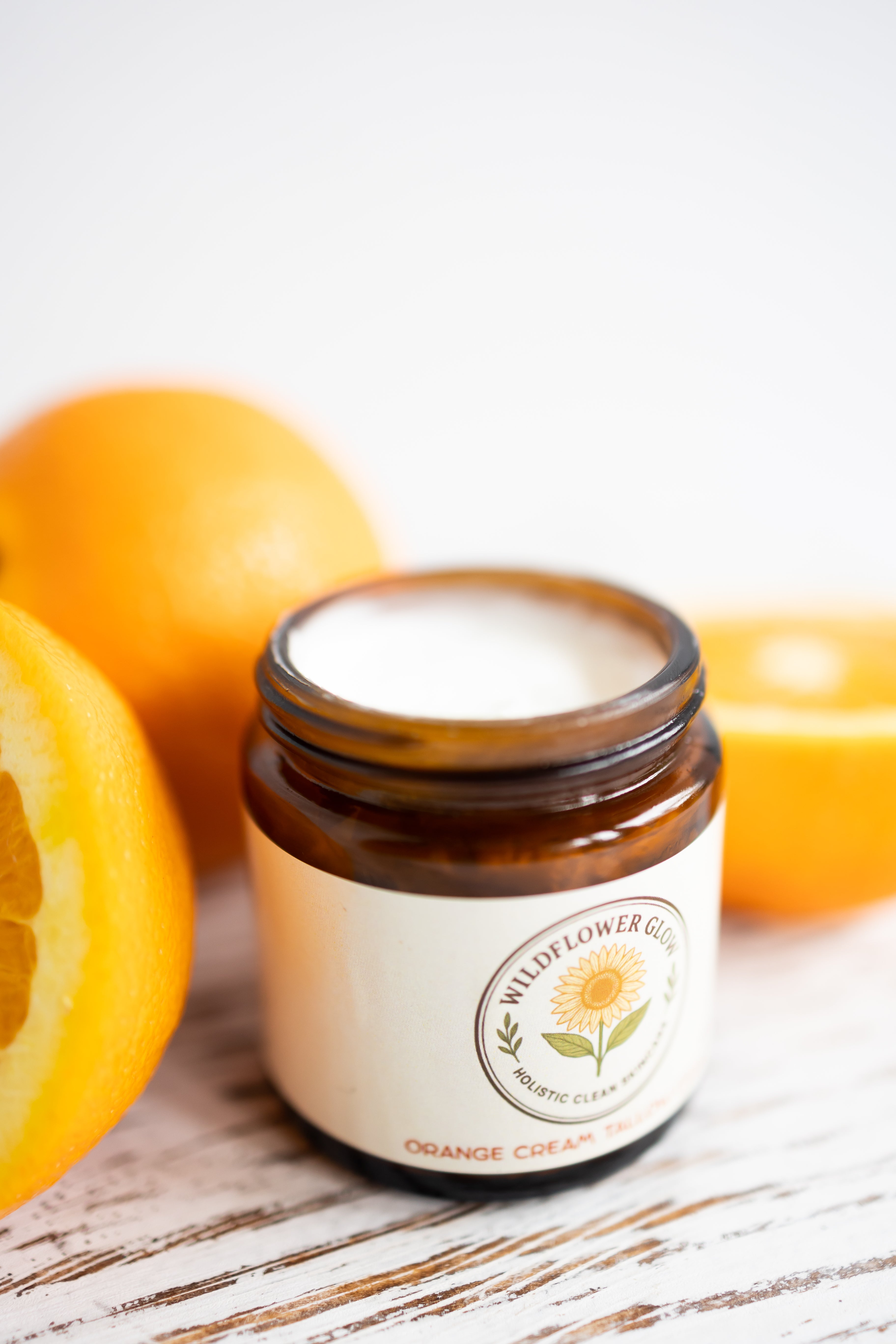 Jar of Wildflower Glow Cream with oranges on a wooden surface