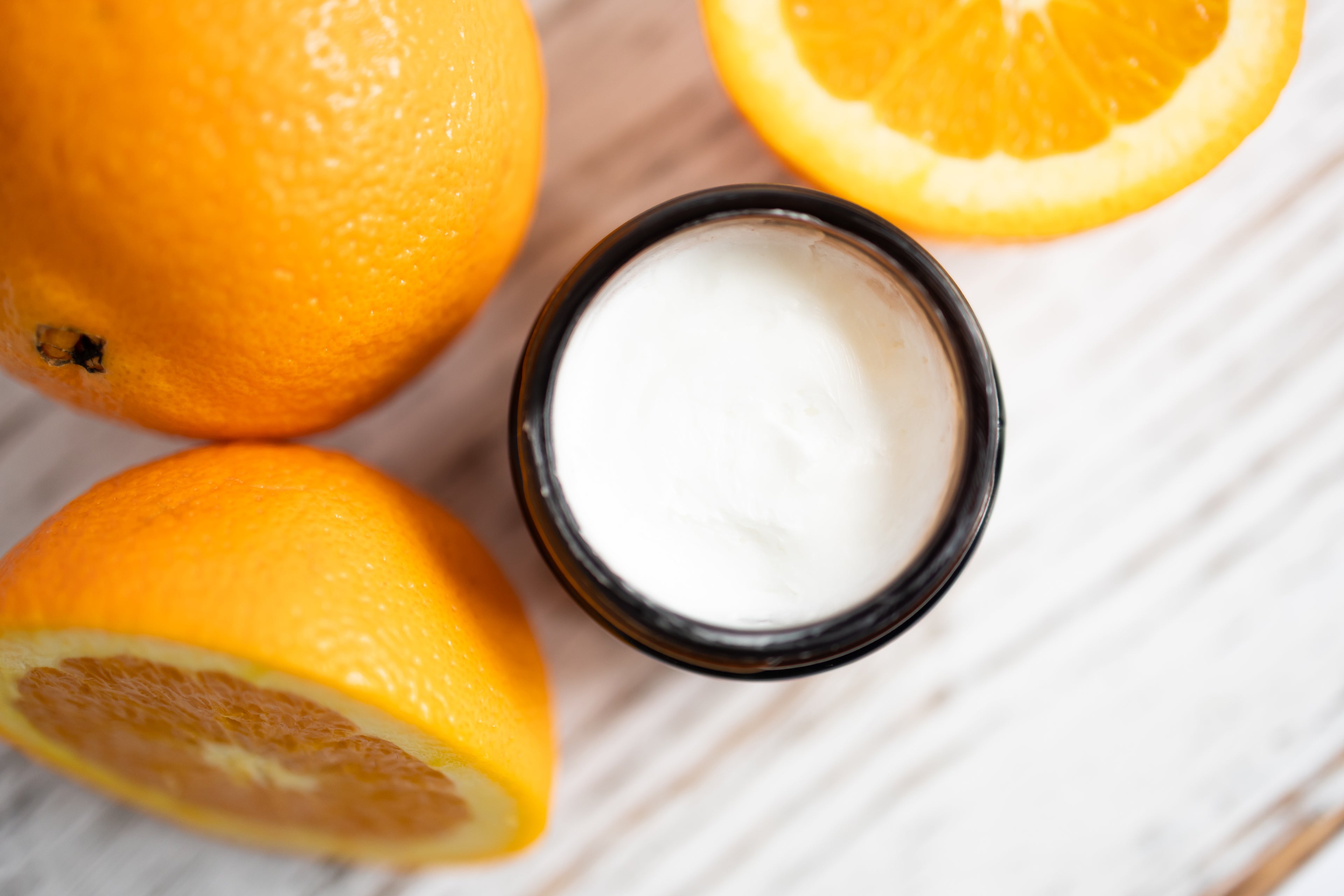 Cream container with sliced oranges on a wooden surface