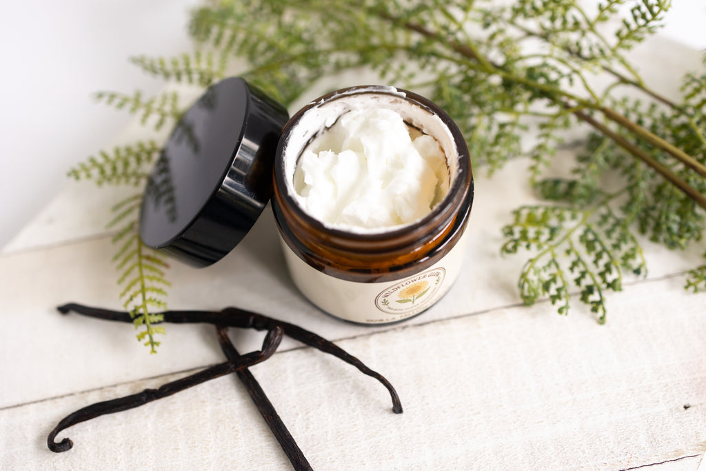 Jar of cream with a black lid on a white surface with greenery
