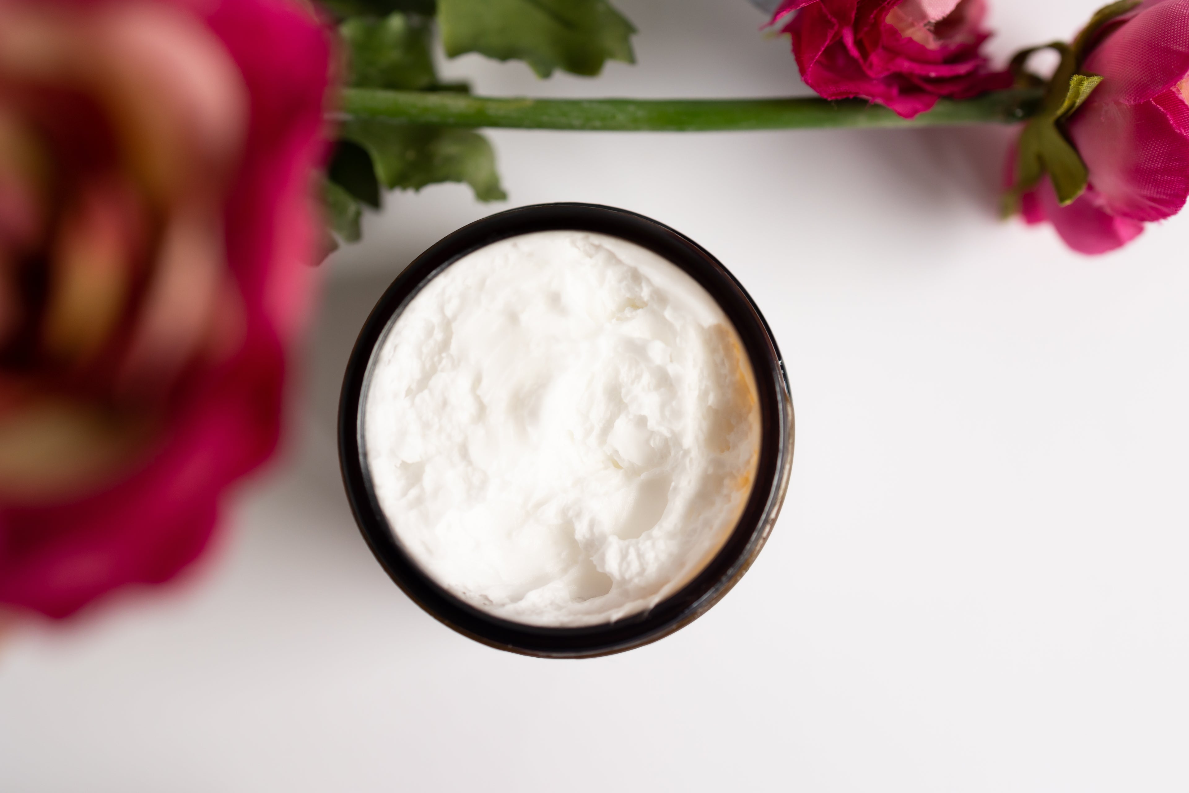 White cream in a brown container with pink roses on a white background