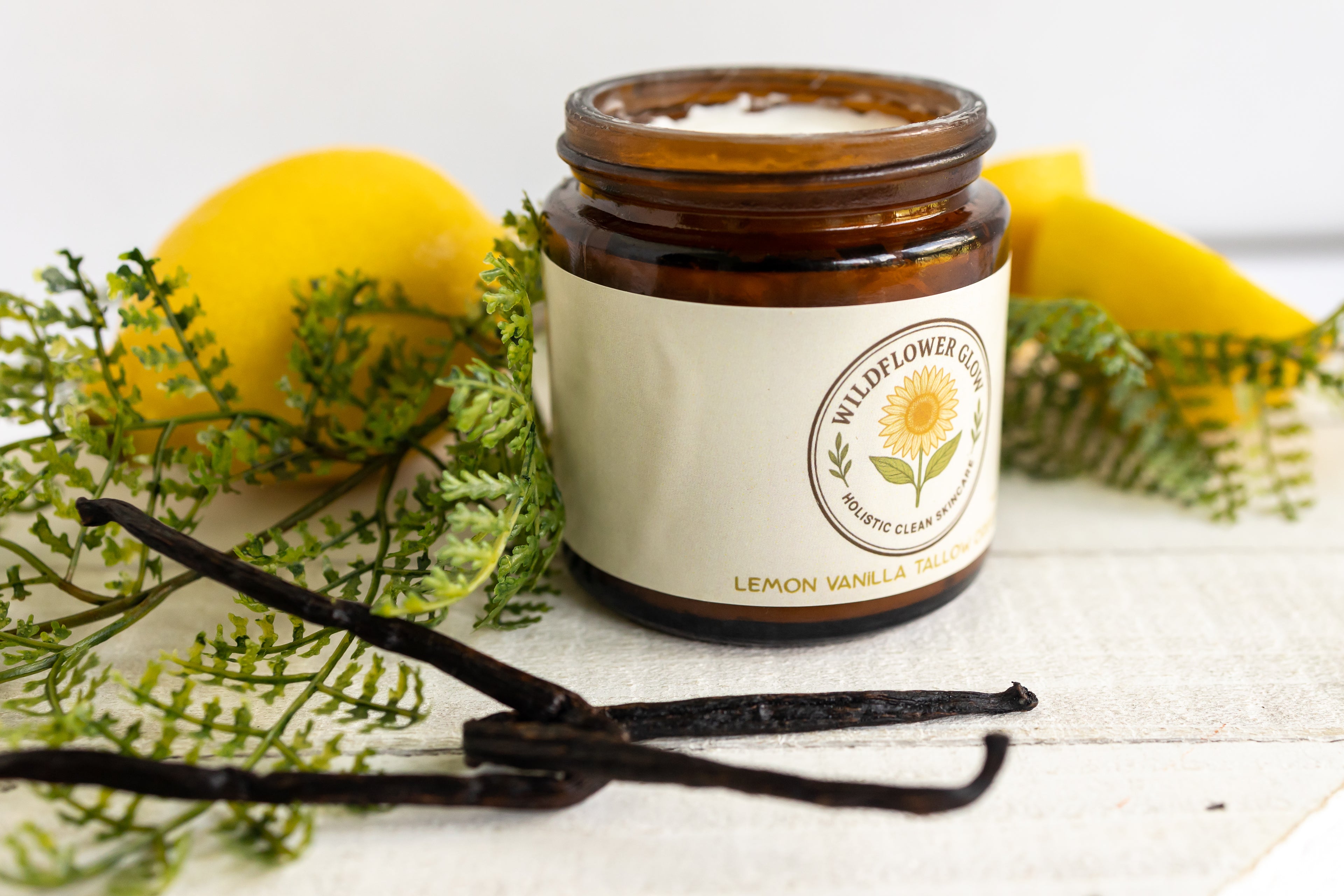 Jar of Wildflower Glow moisturizer with lemon, vanilla beans, and greenery on a white surface
