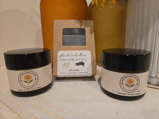 Two moisturizing creams, one with magnesium, surrounding a packaged charcoal and tea tree soap bar. 