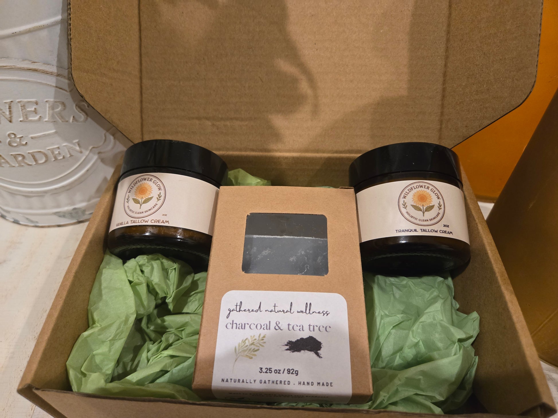 Open box with a vanilla tallow cream, packaged charcoal and tea tree soap bar and a tranquil magnesium tallow cream. 